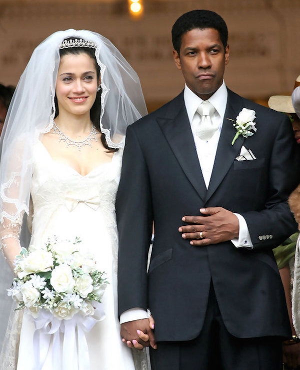 Frank Lucas’ wedding attire features a white-on-white shirt and tie combination beneath a black peaked lapel, single-breasted suit with satin facings, topped off with a white boutonnière in his left lapel and a white silk handkerchief trimmed with black in his breast pocket.