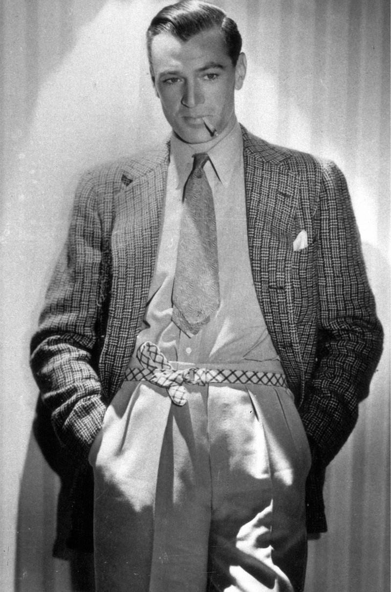 A slicked back Gary Cooper sporting an interesting checked belt to support his high-waisted, forward facing pleated trousers, circa 1937.