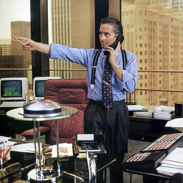 Michael Douglas as Gordon Gekko in the 1987 classic Wall Street. He wears windowpane pleated trousers, supported with two-tone braces for a formal business look.