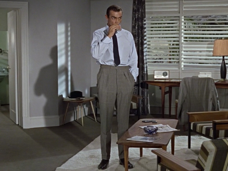 The inimitable Sean Connery as James Bond in Goldfinger, 1964. Connery went to tailor Anthony Sinclair for his drape cut suits, and no doubt his traditional pleated trousers. Here, he wears a style known as English pleats, in sharkskin grey flannel.