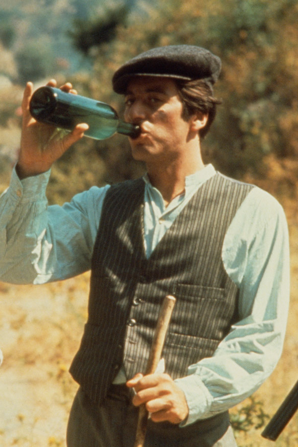 During the scenes in Sicily, the exiled Michael Corleone's workwear consists of a grey pinstriped waistcoat and trousers over a pale blue Mandarin-collar shirt and a grey peaked cap.