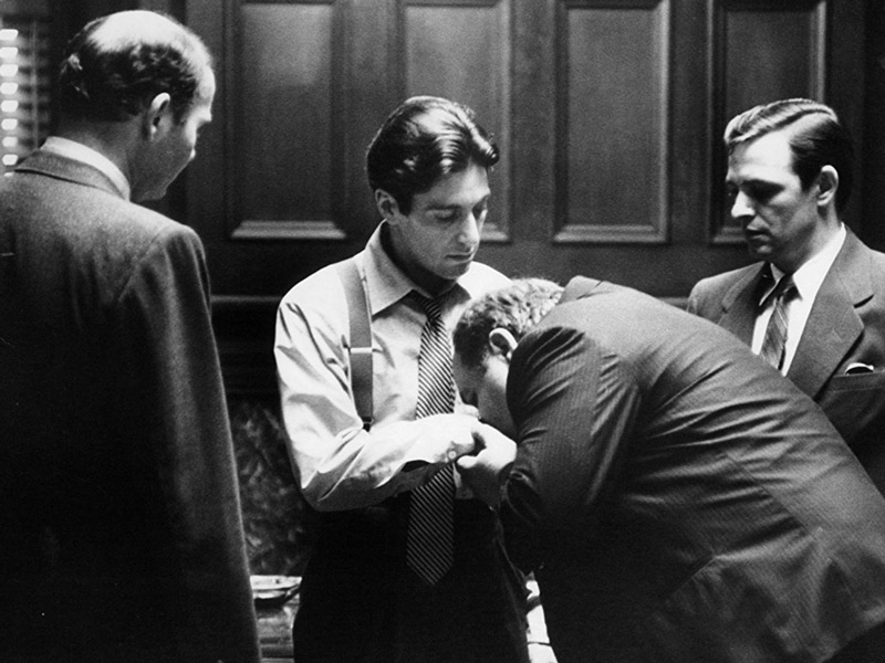 The closing scene shows Michael Corleone wearing shirtsleeves in a white business shirt with a loosened black-and-silver striped, smooth silk tie.