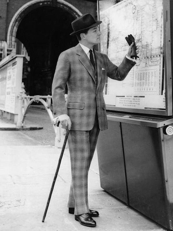 A finely dressed gentleman checks the train timetable wearing a suit cut in oversized checked cloth.