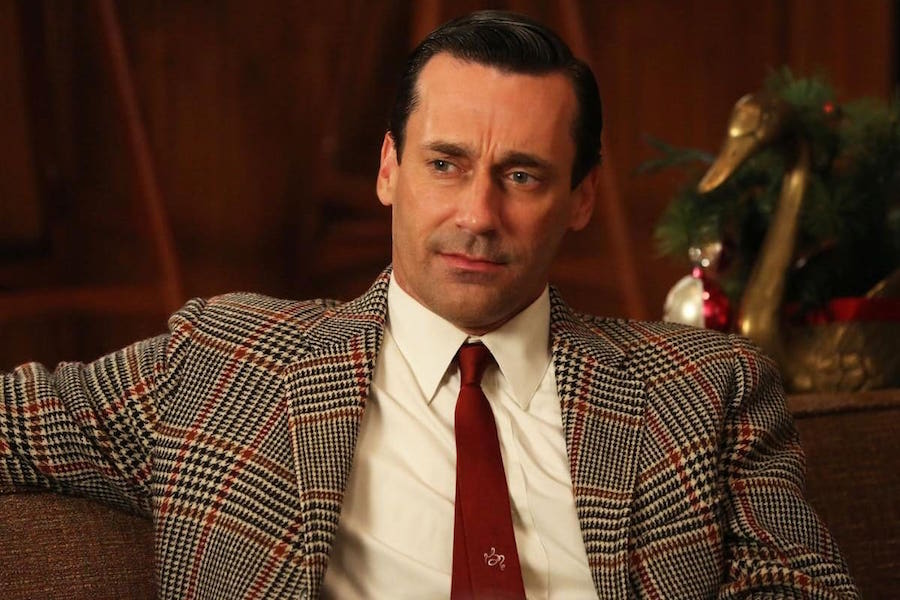 Jon Hamm in Season 6 of Mad Men, wearing a bold sports coat with a red overcheck, paired with an embroidered insignia tie.