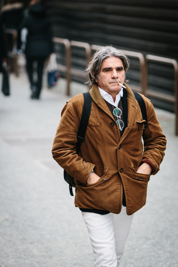 A backpack worn over a preppy, Ivy League-inspired ensemble of white trousers with a crew neck and open collar shirt. Photo by Jamie Ferguson.