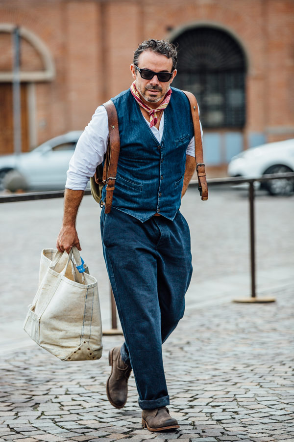 The vintage feel of a collarless shirt, denim waistcoat and pleated turn-ups is underlined by a well-worn canvas backpack with leather accents. Photo by Jamie Ferguson.