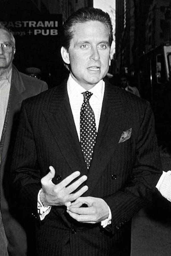 Wearing a double-breasted pinstriped suit over a horizontally-striped shirt, spotted tie and pocket square, Gekko holds his signet ring in a traditional power stance. Photograph by Ron Galella/WireImage.