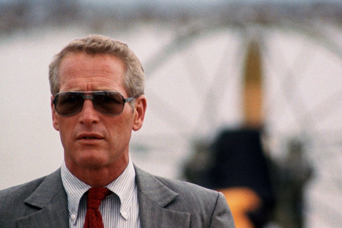 Paul Newman dons a striped button-down shirt with a red tie under a grey suit, finished with sunglasses in The Drowning Pool, 1975.