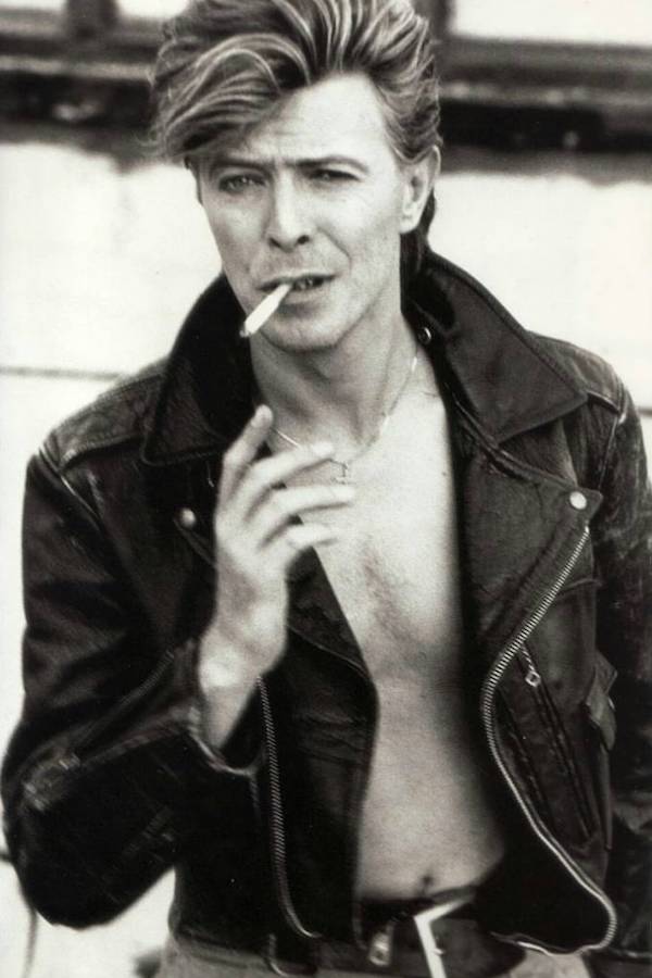 David Bowie dons a leather motorcycle jacket in true rock star style, worn open with no shirt underneath and a cigarette casually hanging from his mouth, circa 1987.