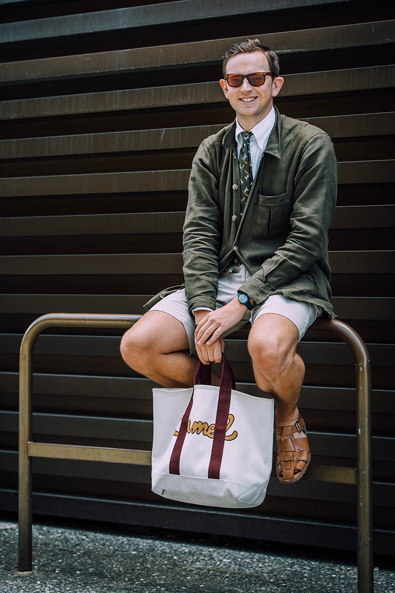 Lucas Nicholson of Drake's sports a smart shirt and tie combo worn with shorts at Pitti Uomo. The olive green jacket and sunglasses make for a very modish aesthetic.