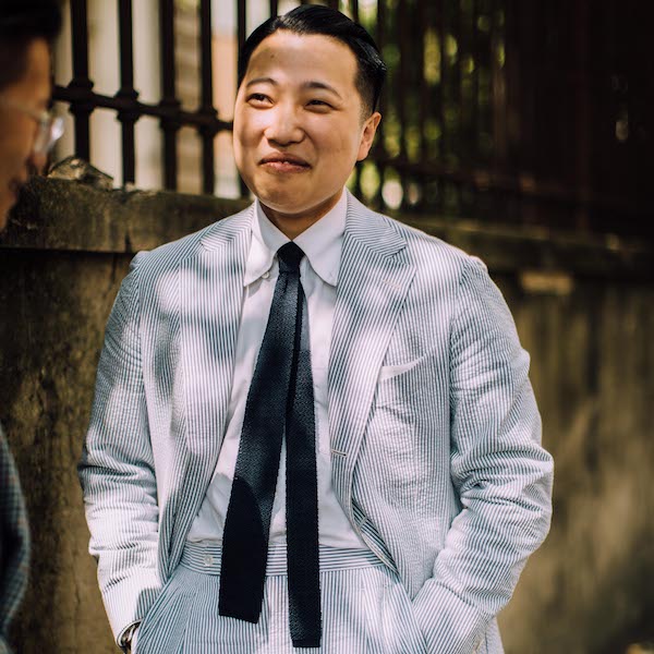 Homie Yang in the classic white/blue Seersucker, paired with a white button-down shirt (worn unbuttoned) and a black knitted tie.