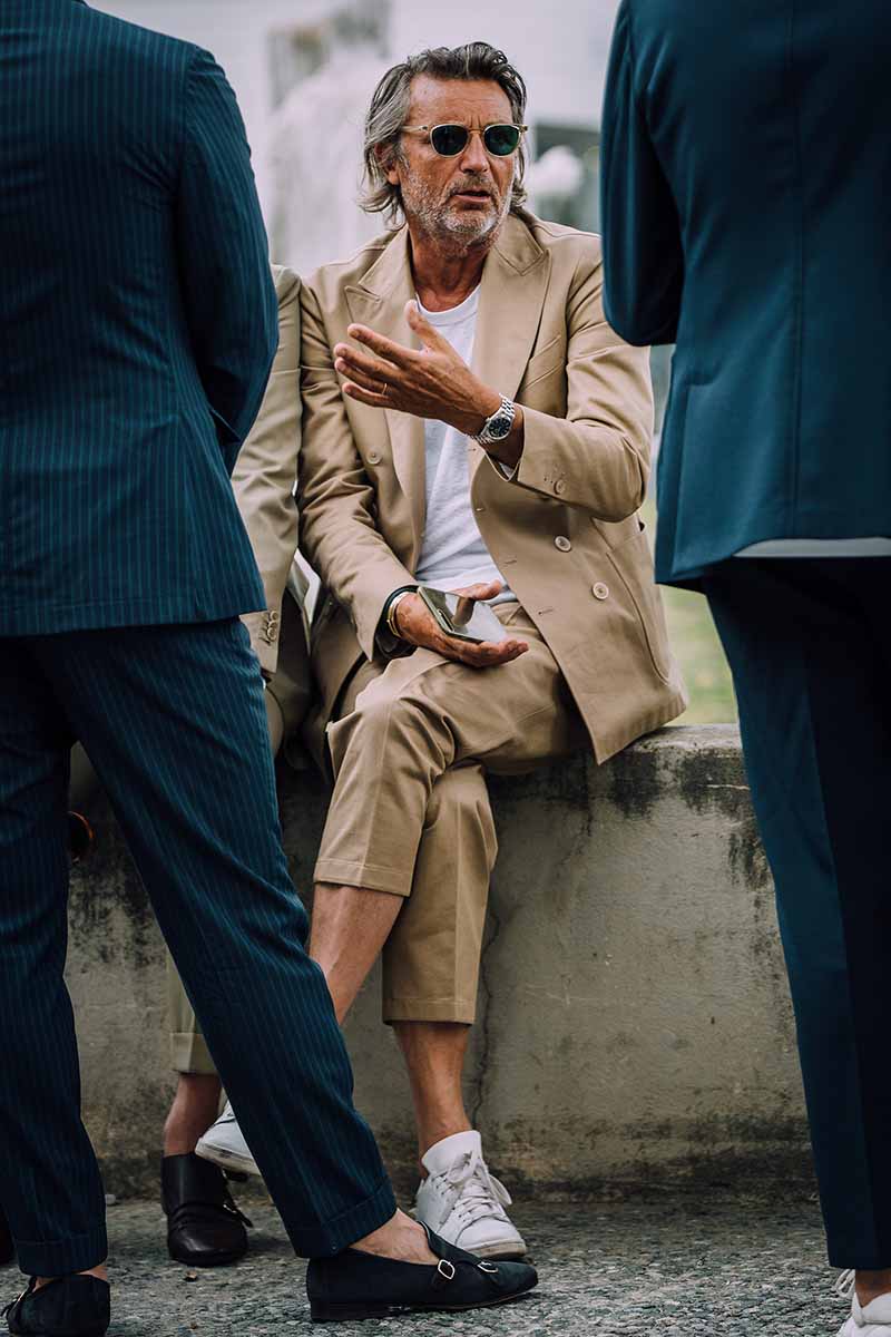 A white T-shirt and white sneakers combo nicely complements the camel tone of this double-breasted suit ; a steel watch and silver-framed sunglasses complete the look.