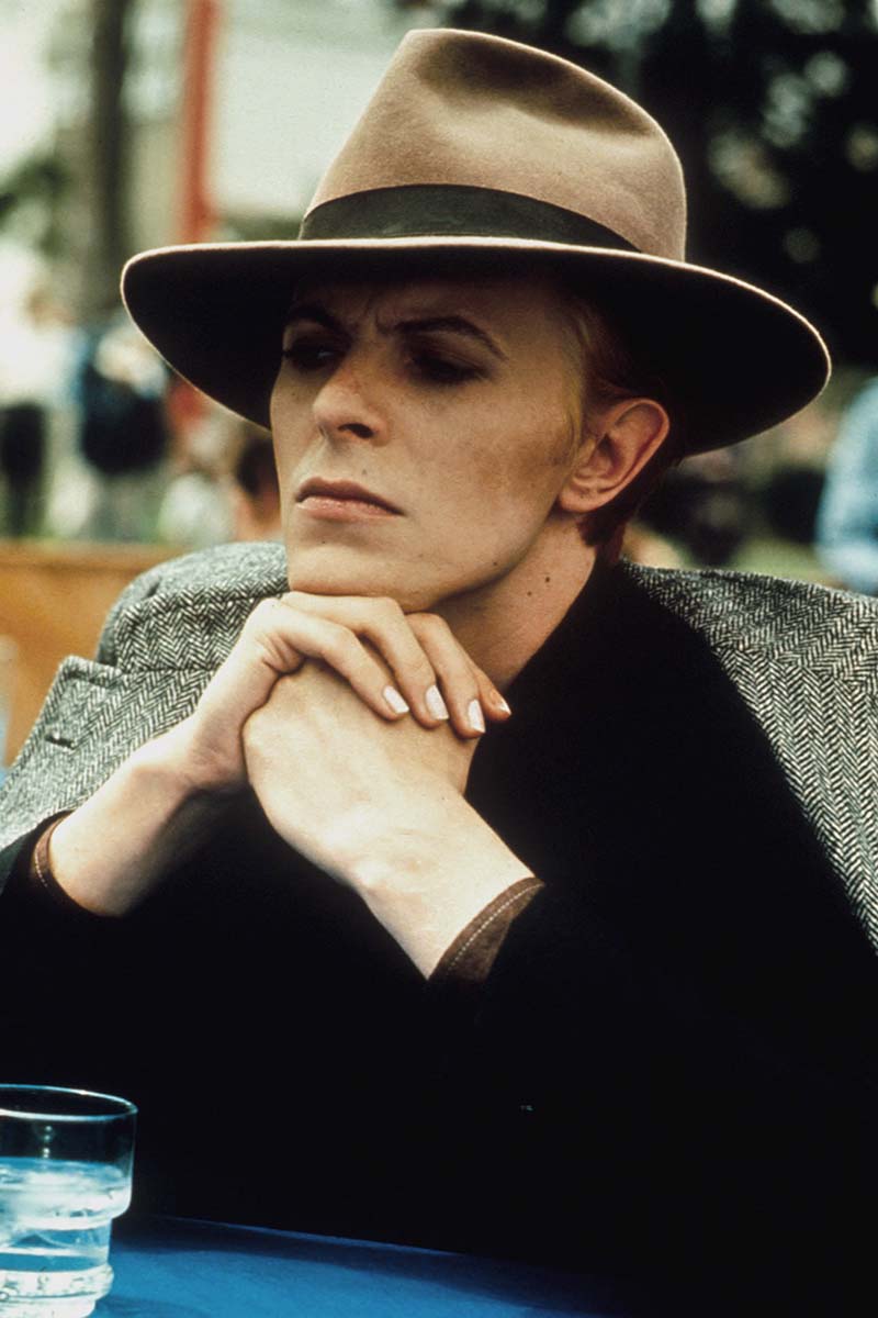 David Bowie in brown Fedora with grey herringbone coat draped rakishly over his shoulders. Photograph by Alamy.