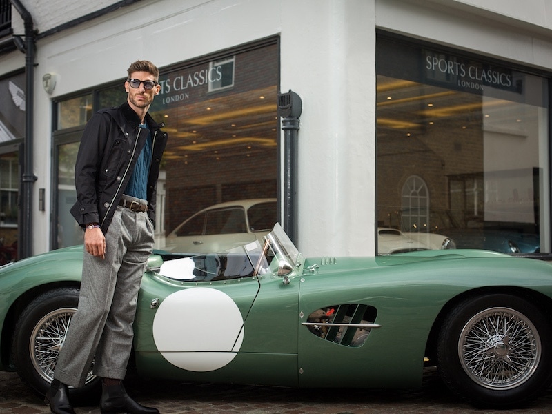 Black single-breasted cloth tourer jacket, Grenfell; Blue cashmere cable knit jumper, Cordone 1956; Grey wool flannel houndtooth wide leg Hollywood Trousers, Edward Sexton; Brown suede belt, Anderson & Sheppard; Black newmarket leather Chelsea boots, Edward Green; 24H Le Mans edition bracelet on blue cord, The Mechanist; Grant polished black sunglasses, Kirk Originals.