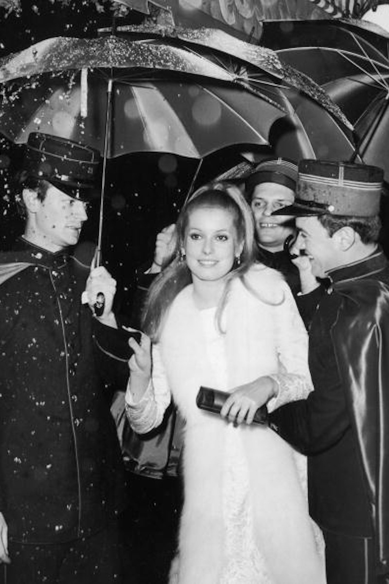 French actor Catherine Deneuve is ushered by gendarmes holding colourful umbrellas at the Little Carnegie Theatre, 57th Street, Manhattan, New York City (Photo by Hulton Archive/Getty Images).