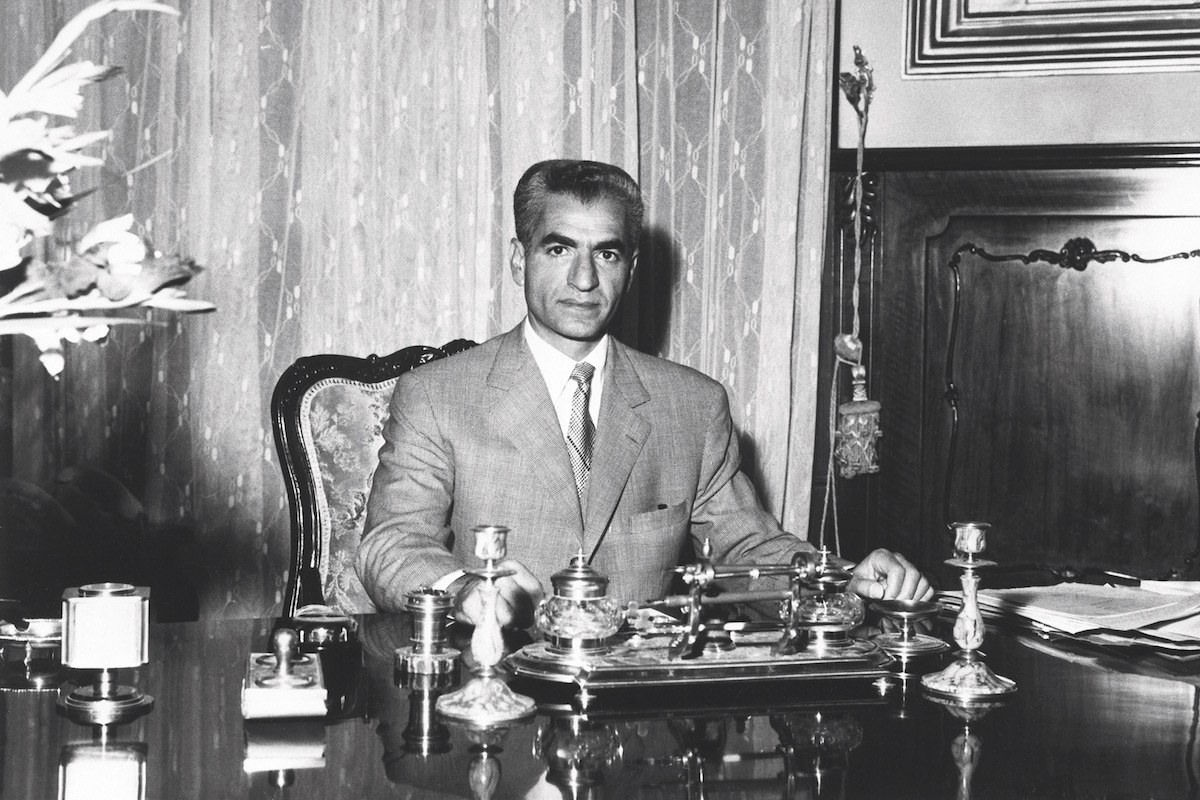 The Shah of Iran seated at a desk. (Photo via Getty)