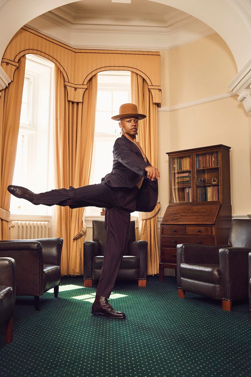 Solomon: Plum wool suit with black stripes and high-waisted trousers, XXX Ermenegildo Zegna; camel cotton T-shirt, Sunspel; Cotswold brown grain calf leather Bryan full brogue derby boot, George Cleverley. Hat and earrings, Solomon’s own.