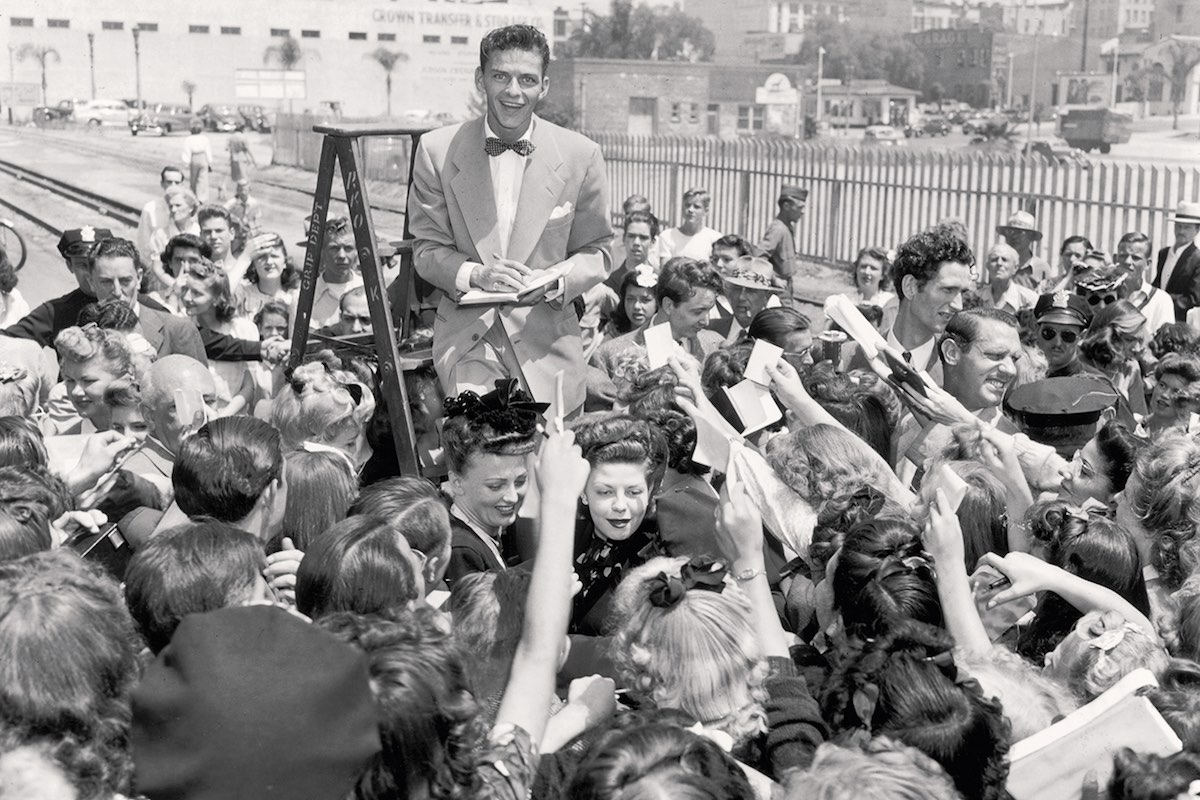 Sinatra stands on a ladder as he signs autographs for a crowd of fans in Los Angeles, 1943 (Photo by Gene Lester/Getty Images)