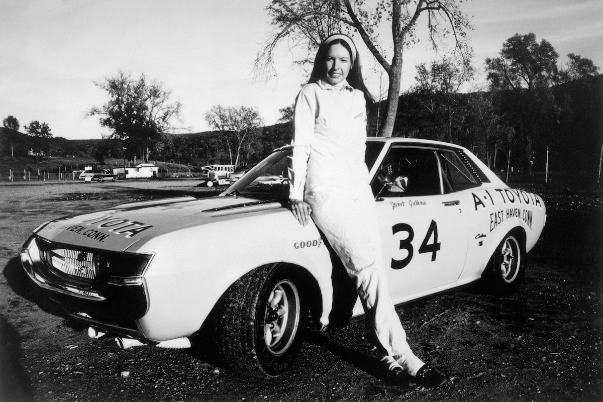 Janet Guthrie leans against her race car.