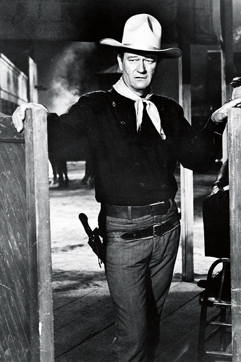 American actor John Wayne (1907 - 1979) wears a Western outfit which includes a pistol in a holster and stands in a doorway in a still from the Cowboy film 'The Man Who Shot Liberty Valance' directed by John Ford, 1962. (Photo by Paramount Pictures/Courtesy of Getty Images)