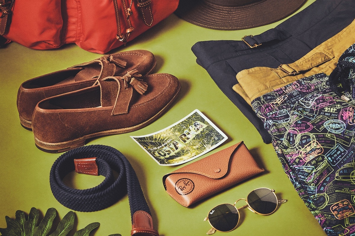 Red leather trimmed nylon backpack, khaki packable cotton trilby and navy cotton elastic woven belt, all Anderson & Sheppard at The Rake; brown snuff suede Solent unlined tassel loafer, Crockett & Jones; military green cotton pleated shorts and navy cotton pleated shorts, both Lardini at The Rake; navy polyamide ‘Passport Please!’ print 50th anniversary 1980s swimwear shorts, Vilebrequin; round metal gold-and-green lens sunglases, Ray-Ban.