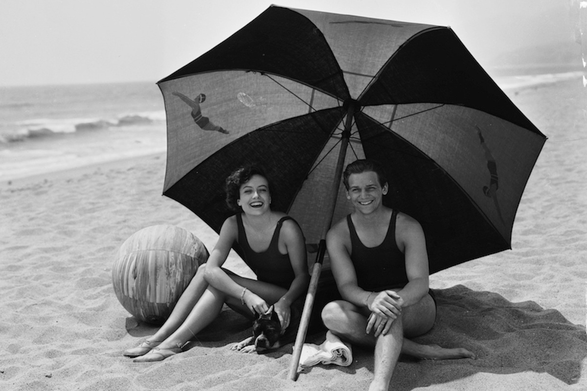 Joan Crawford shares the shade of a large striped beach umbrella with her second husband, actor Douglas Fairbanks Jr (Photo by Clarence Sinclair Bull/John Kobal Foundation/Getty Images)