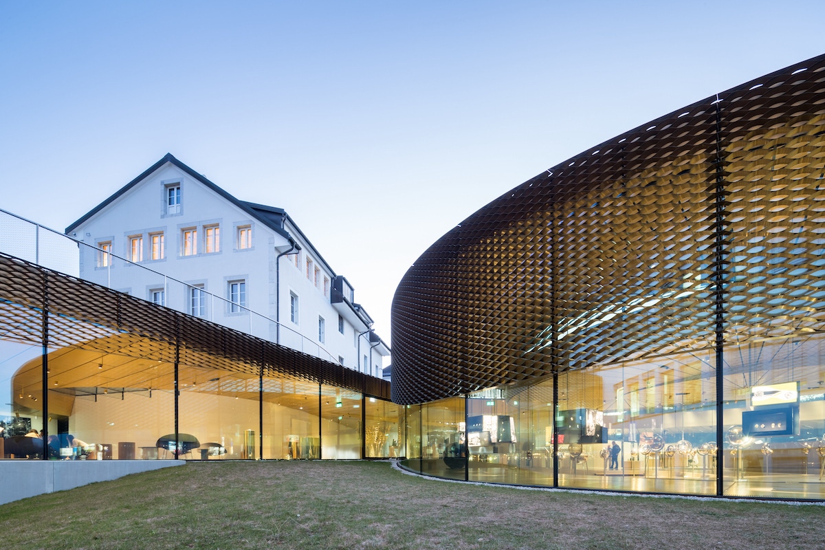 The spiral structure is supported by curved glass walls. A brass mesh runs along the exterior to regulate temperature and light, without obstructing the view.
