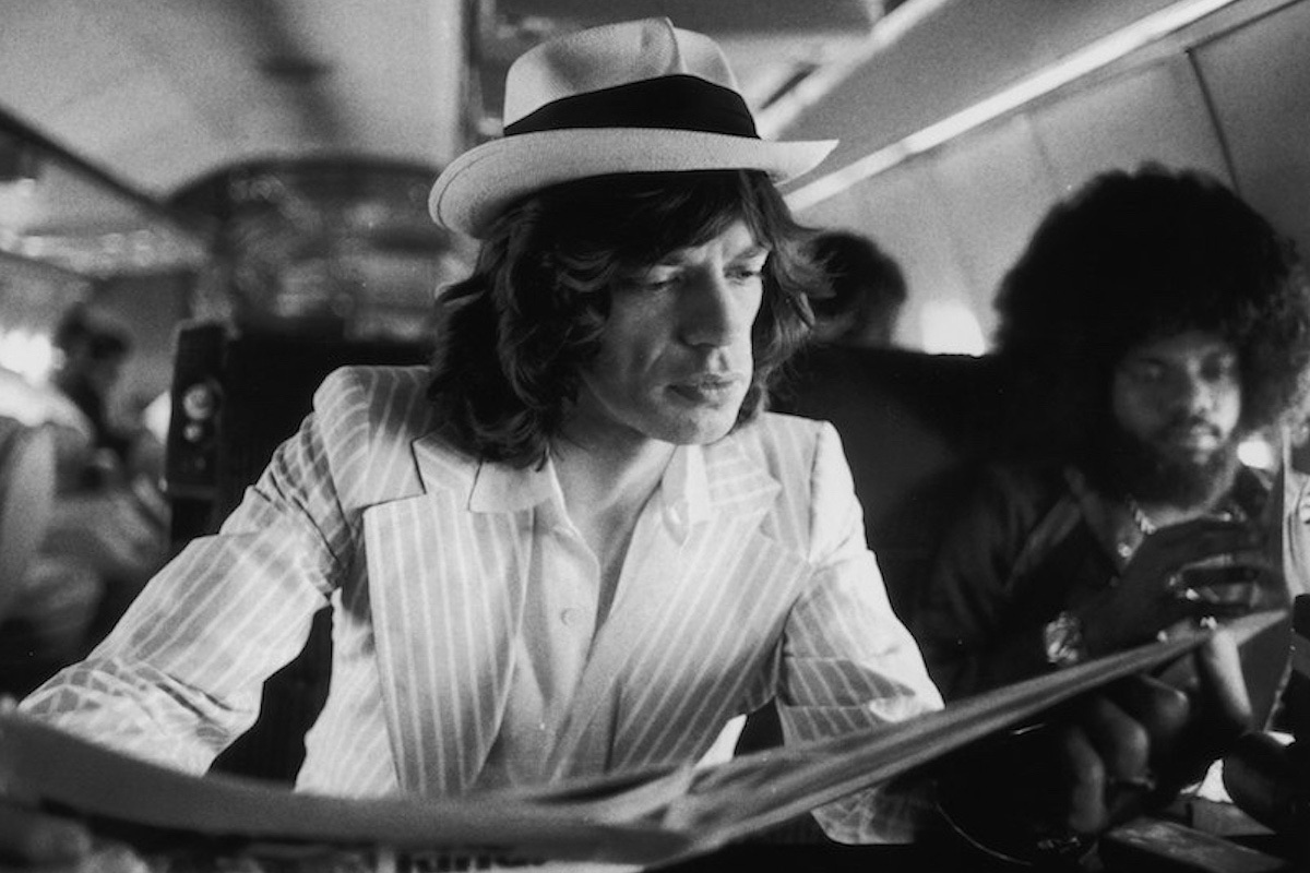 Mick Jagger keeps abreast of current affairs while travelling between concerts in the Rolling Stones' private jet during their 1975 Tour of the Americas. (Photo by Christopher Simon Sykes/Hulton Archive/Getty Images)