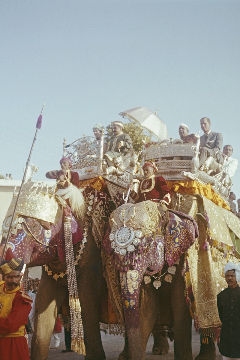 Queen Elizabeth II smiles as she rides in an elaborate howdah alongside Prince Philip (right) on the backs of two ornately decorated elephants through the city of Benares (Varanasi), during her Commonwealth tour of India in February 1961. Sitting beside Prince Philip is Prime Minister of India Jawaharlal Nehru. (Photo by Rolls Press/Popperfoto via Getty Images/Getty Images)