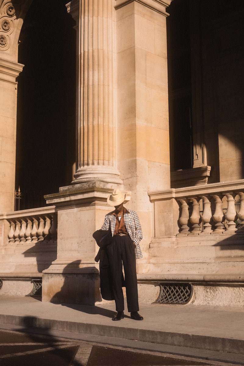 Kevis wears: blue, beige and gold linen, silk, wool and cotton blend gun club check jacket, Stile Latino at The Rake; chocolate brown silk shirt, Edward Sexton at The Rake; black and navy virgin wool macro double-breasted Albert overcoat, MP Massimo Piombo; hat, trousers, boots and vest, models own.