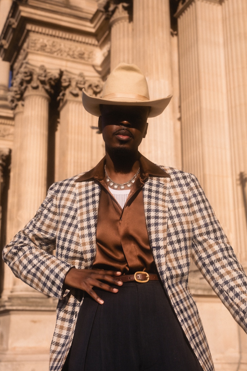 Kevis wears: blue, beige and gold linen, silk, wool and cotton blend gun club check jacket, Stile Latino at The Rake; chocolate brown silk shirt, Edward Sexton at The Rake; hat, trousers, boots and vest, models own.