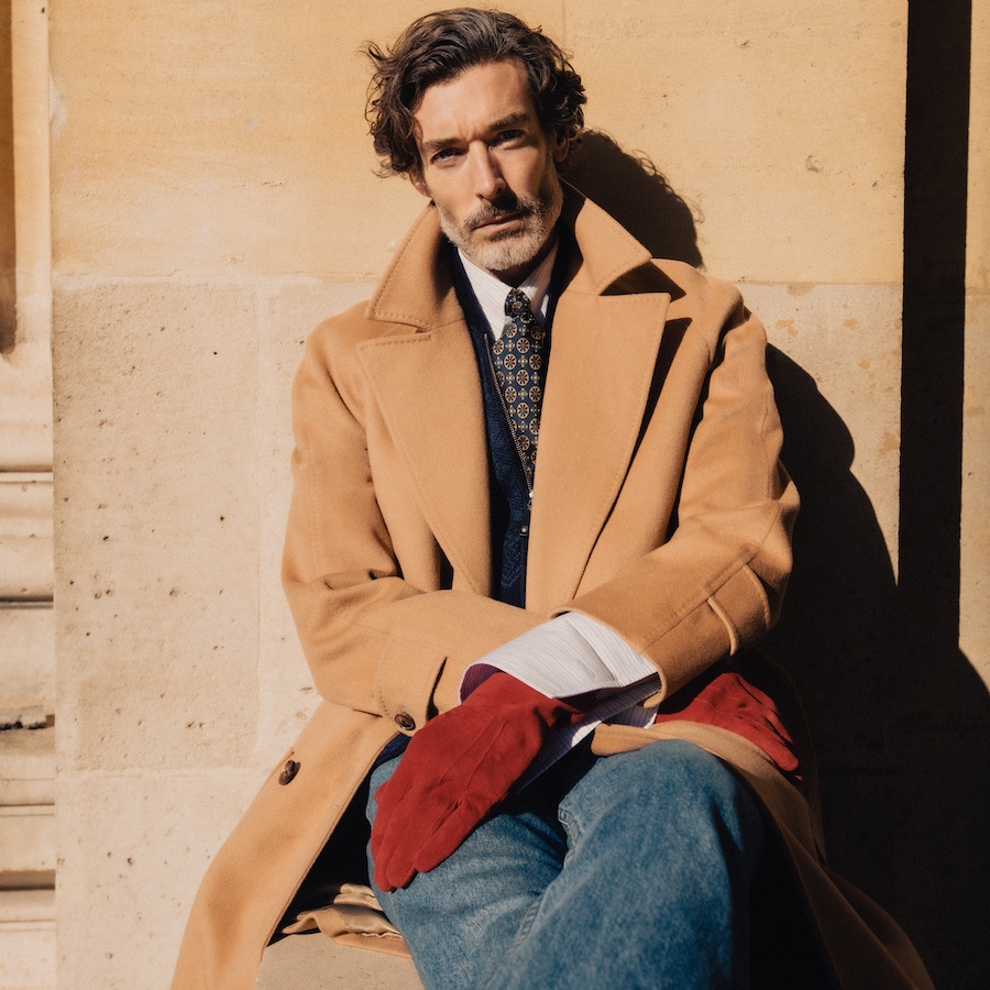 Richard wears: Camel wool Raglan coat, white, red and blue cotton striped pin collar shirt, both Edward Sexton at The Rake; knitted Fair Isle car vest, Connolly; red soft suede leather gloves, Anderson & Sheppard; denim, loafers and tie, models own.