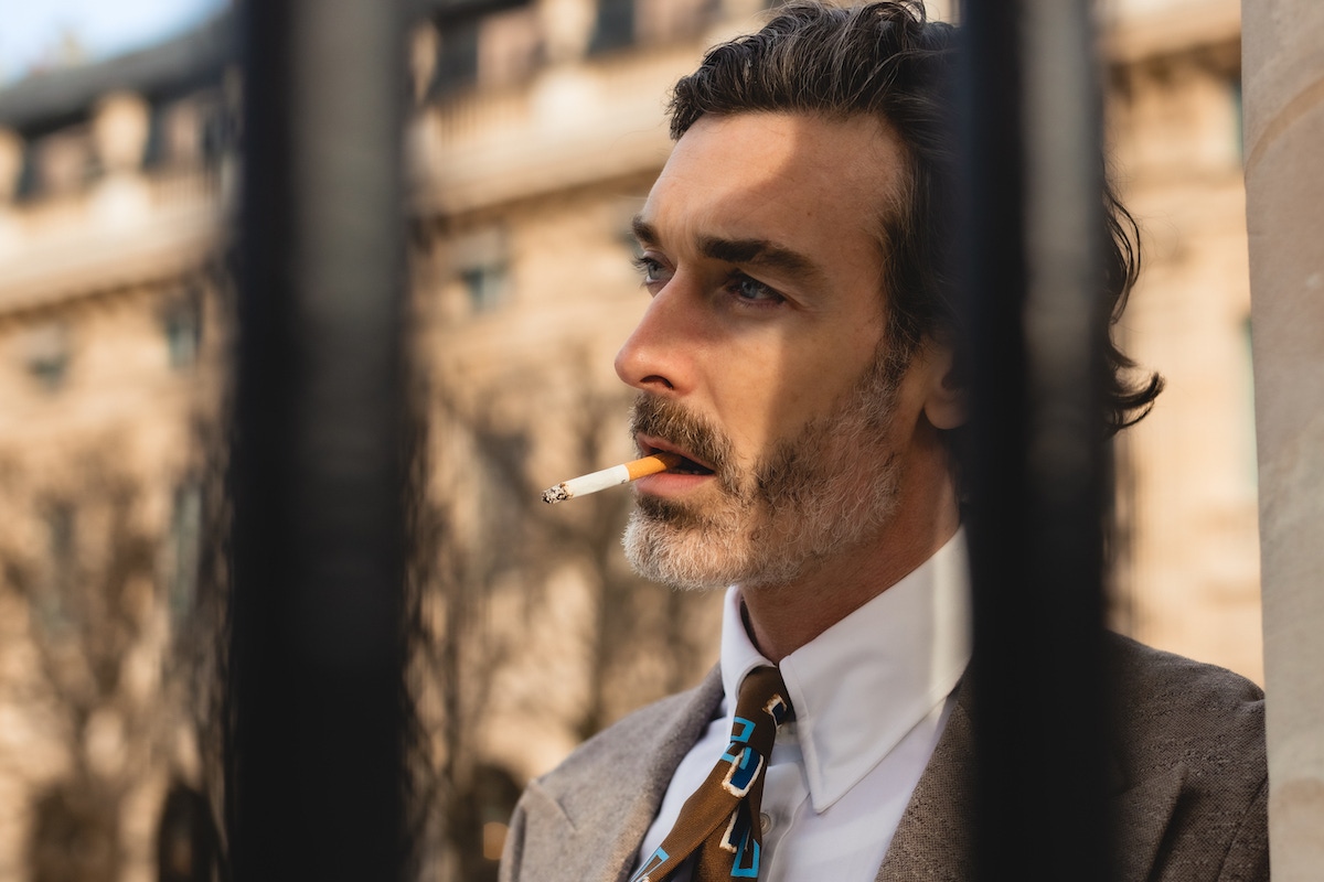 Richard wears: Beige wool Jersey unstructured single-breasted jacket, white cotton pin-collar shirt, both Edward Sexton at The Rake; brown, blue and white rectangle print silk tie, Lorenzo for The Rake at The Rake; trousers, belt and boots, models own.