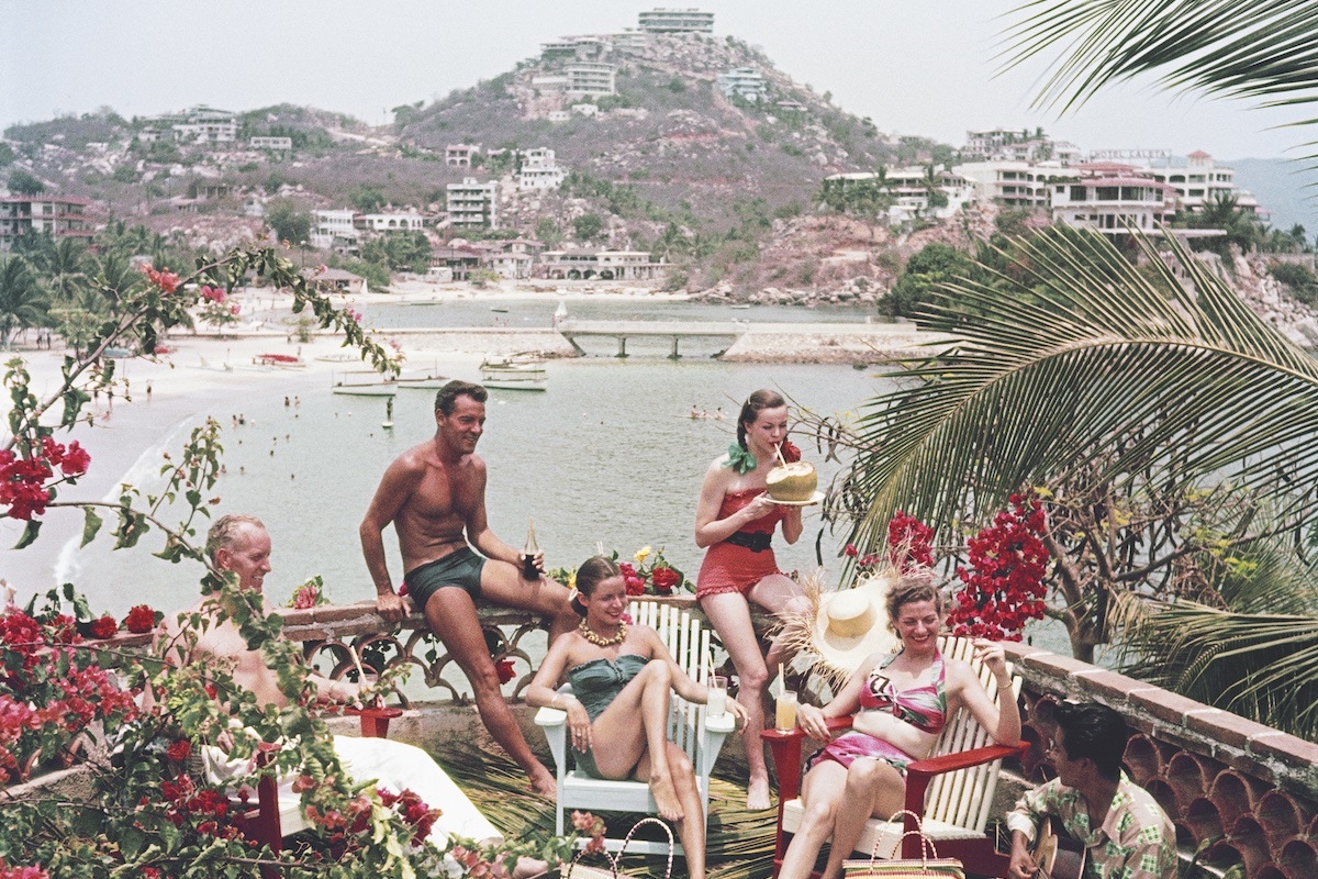 Bill Babb, Thomas Beecher, model Carolyn Phillips, Mrs Rabb and model Jean Adams enjoy some guitar music on a terrace in Acapulco, 1952 (Photo by Slim Aarons/Hulton Archive/Getty Images)